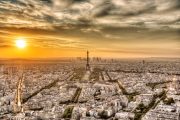 Panoramic view of Paris with the Eiffel Tower at sunset, under a dramatic sky.