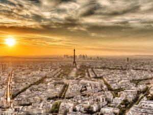 Panoramic view of Paris with the Eiffel Tower at sunset, under a dramatic sky.