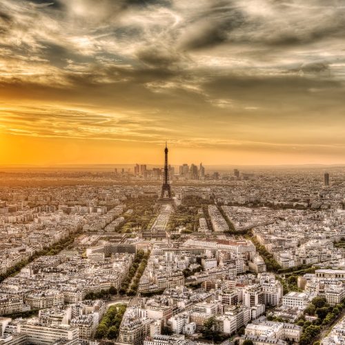 Panoramic view of Paris with the Eiffel Tower at sunset, under a dramatic sky.